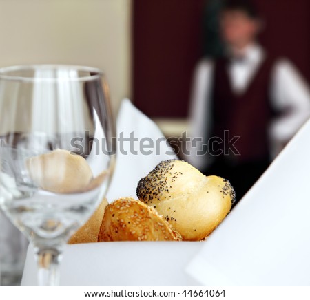 table setting in restaurant with bread empty glass and waiter off focus