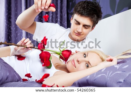 romantic couple in bed, female holding red rose, male releases  petals