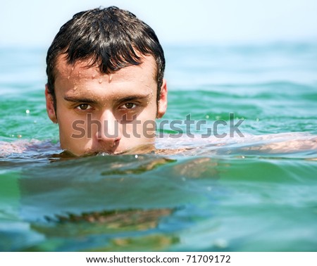Close-up of young handsome male face in water, looking at camera
