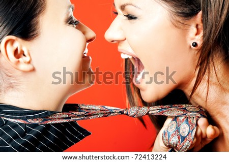 Close-up of two females facing each other, one pulling other on necktie screaming with excitement