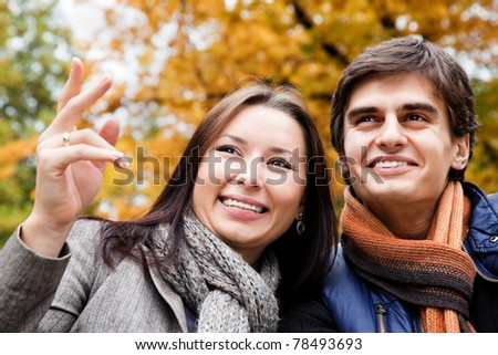 Close-up of happy couple smiling in park on an autumn day, female pointing