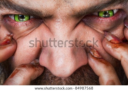 Cropped image of scary man\'s face with green artificial eyes and bleeding fingers