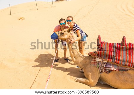 Young couple standing near a camel in a desert taking photo with it near Dubai