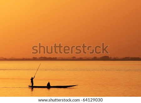 Silhouette of African fisherman in canoe at sunset