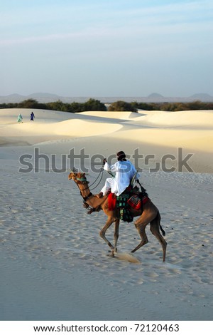 A Tuareg nomad riding his camel in the Sahara desert with two women in the background