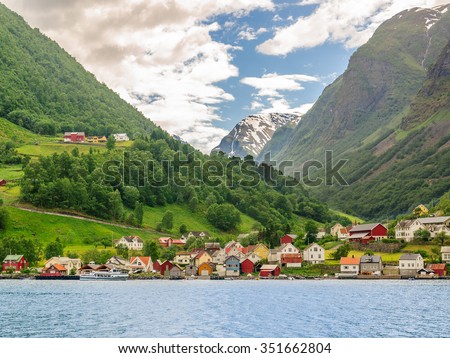 A lots of little colorful traditional Norwegian houses near the sea with green forest on mountains on background and blue sky with dark clouds, Sognefjord, Norwa