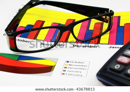 Colorful sales charts, calculator, blue pen and glasses. Shallow, focus on charts