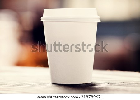 Disposable coffee cup on windowsill with city in background.