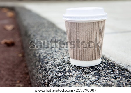 Disposable coffee cup on sidewalk with city in background.