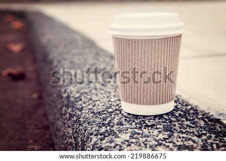 Disposable coffee cup on sidewalk with city in background.