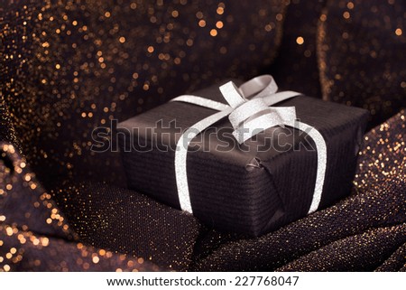 Black gift box with silver bow on black shiny background.