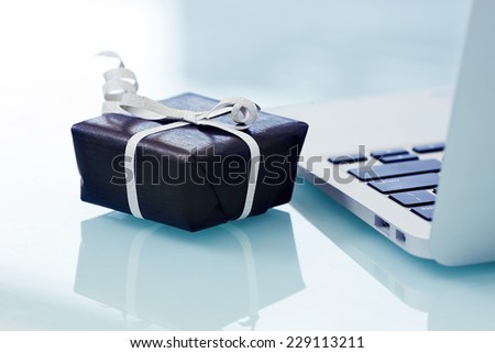 Black gift box with silver bow on light background next to the computer. On line shopping