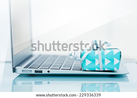 Gift box with silver bow on light background next to the computer. On line shopping