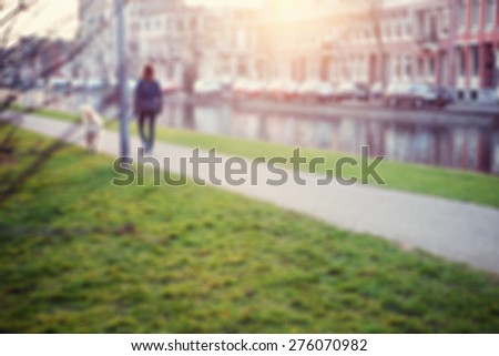 Blurred image of the city. Amsterdam canal view with a woman walking his dog on a pathway.