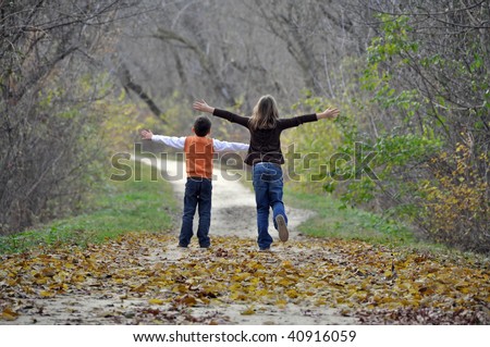 two children playfully run down a tree lined path on a beautiful autumn day
