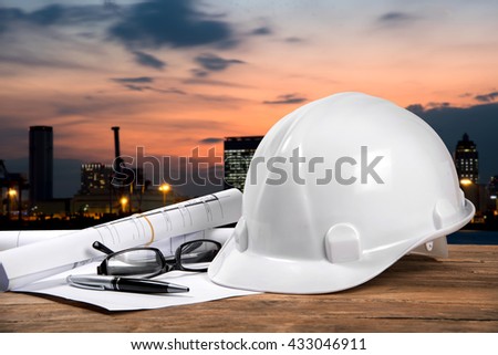 safety helmet and architect plant on wood table with city sunset scene and building construction