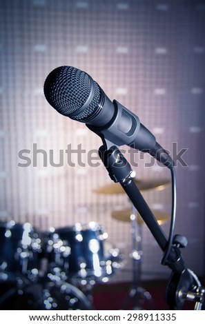 Modern microphone on a stand, recording studio, microphone picture, sound wall, microphone stand, drum set, mesh wire, close-up shot, vertical image, images in dark colors.