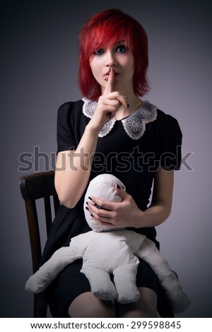 Red-haired girl, dress with lace collar, rag doll, calls for silence, sitting on a chair, hugging a doll, blue eyes, vintage image, vertical photo.