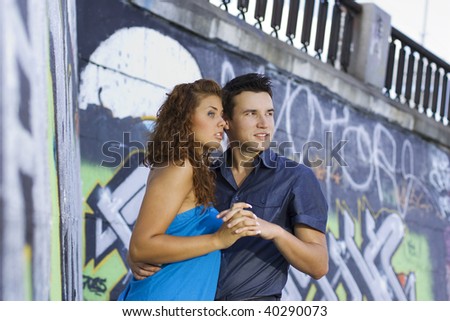 Young couple holding hands against graffiti wall.