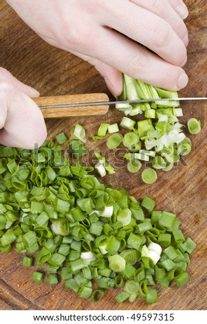 A chopped green onions on a wooden chopping board with a knife.