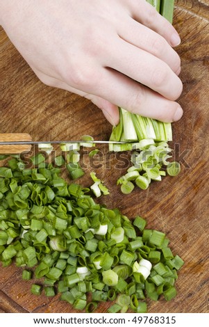 A chopped green onions on a wooden chopping board with a knife.