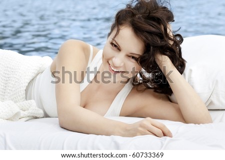 Beautiful young woman lying on the white bed in the sea