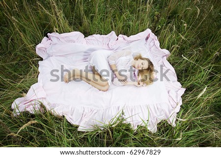 Portrait of a woman lying on a pink sheet in a green field