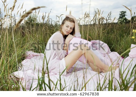 Portrait of a woman lying on a pink sheet in a green field