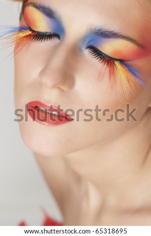 Beautiful woman with face framed in feathers with bright makeup and long faux lashes