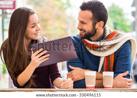 Young man and woman talking , they have fun , they have in their hands the tablet . They drink coffee or tea