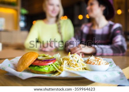 two girl - eating hamburger and drinking  in a fast food diner; focus on the meal