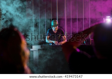 Charismatic disc jockey at the turntable. DJ plays on the best, famous CD players at nightclub during party. EDM party concept.