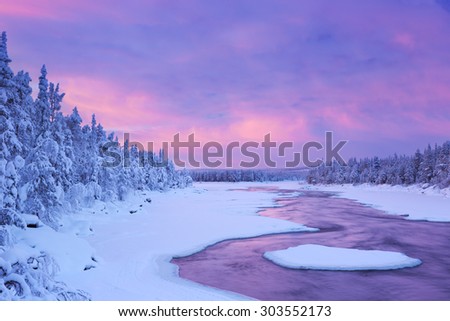 A rapid in a river in a wintry landscape. Photographed at the rapids in the Muonionjoki river in Finnish Lapland at sunrise.