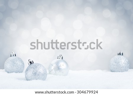 Silver Christmas baubles on snow with defocused silver and white lights in the background. Shallow depth of field.