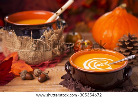 A bowl of homemade creamy pumpkin soup on a rustic table with autumn decorations.