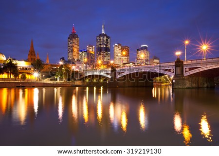 The skyline of Melbourne, Australia with Flinders Street Station and the Princes Bridge from across the Yarra River at night.