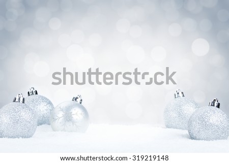 Silver Christmas baubles on snow with defocused silver and white lights in the background. Shallow depth of field.