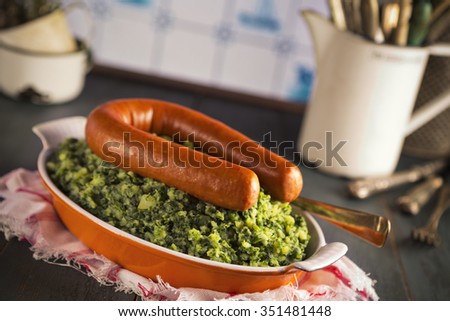 A rustic kitchen with a dish with \'Boerenkool met worst\' or kale with smoked sausage, a traditional Dutch meal. With typical Dutch Delft blue tiles on the wall in the background.