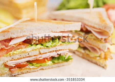 A club sandwich on a rustic table in bright light.