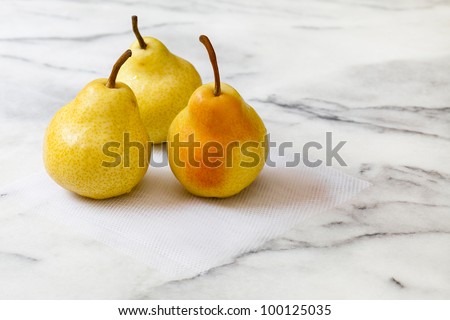 Three fresh yellow pears with pink blush, on a white marble counter top.  The pears are sitting on a square of white tulle netting.