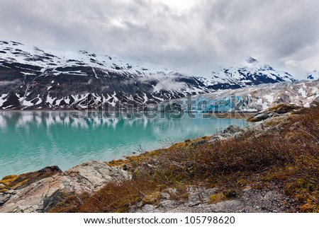 Glacier landscape in Alaska with blue ice reflected in a lake of glacial melt. Glacier Bay wilderness.