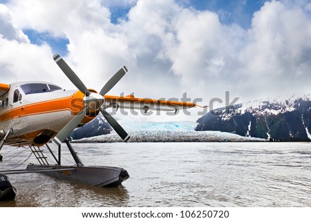 Seaplane or float plane in Alaska. The plane has landed under stormy skies near a glacier.