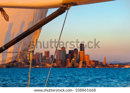 Sunset cruise with a sail framing the Seattle skyline in the background.  You can see shadows on the sail of people on the boat.  Copy space