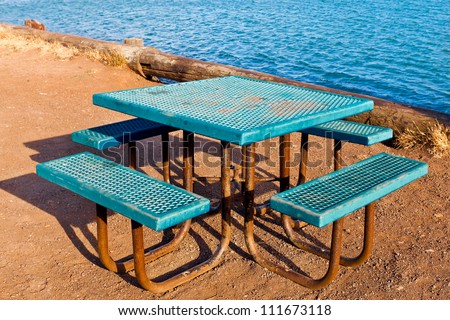Picnic table.  Retro looking square metal table with attached benches in turquoise blue textured metal. Location is next to open water.