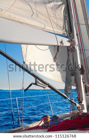 Sailing, with closeup of sail, rigging and ropes.  Sail lit by the bright afternoon sunlight.