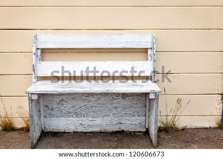Rustic wooden outdoor cottage bench painted white against a butter yellow wood plank wall.