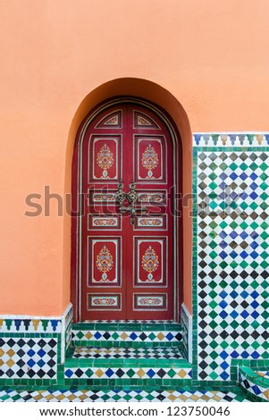 Moroccan painted exterior arched wooden door in red with floral designs and ornate hardware.  Location: Marrakech, Morocco