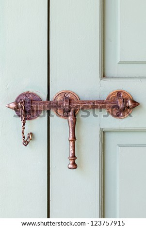 Ornate copper and brass door latch hardware from Morocco on a pale green wooden door.  Close up detail.