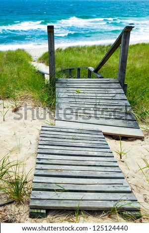 Wooden path down to the beach and ocean.  Walkway and stairs through sand dunes and grass.