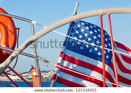 Sailboat steering wheel, orange life preserver and an American flag.  Close up of items on a typical American sailboat or yacht out for a sail.